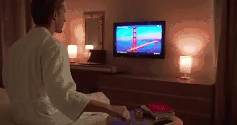 动图：穿浴袍的人坐在床边，抬手控制对面的电视
